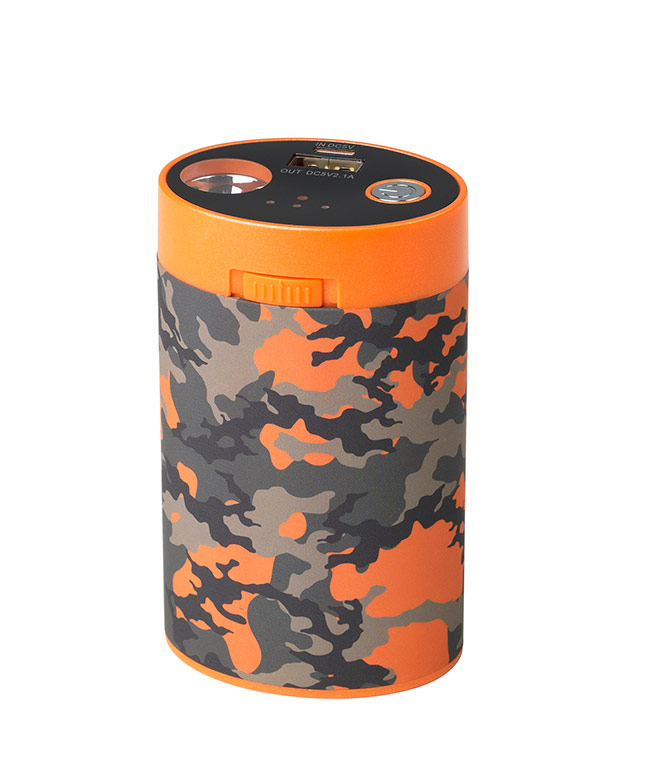 Camouflage-patterned cylindrical battery pack with orange details and charging plug. Use with heated clothing in outdoor activities.