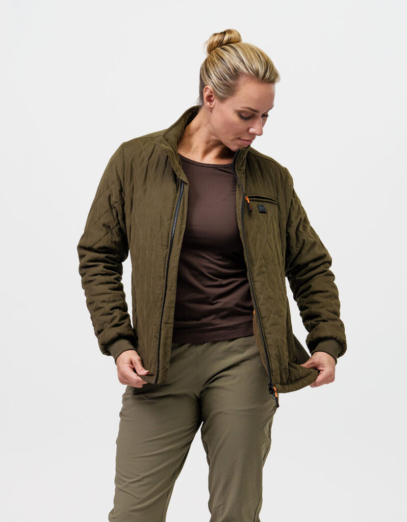 A woman wearing NordicHeat thermal clothing adjusts a green jacket. The jacket promotes active lifestyle through functional insulation and modern design. Visible text: None.