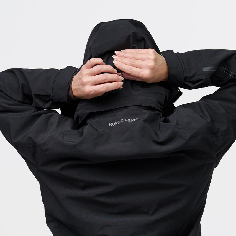 Person adjusts the hood of a black jacket with the text "NORDICHEAT™" on the back, against a solid color background.