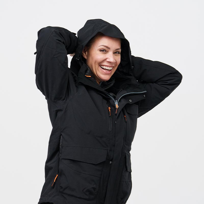 A person wearing a black hooded NordicHeat winter jacket is smiling in a studio setting with a white background.