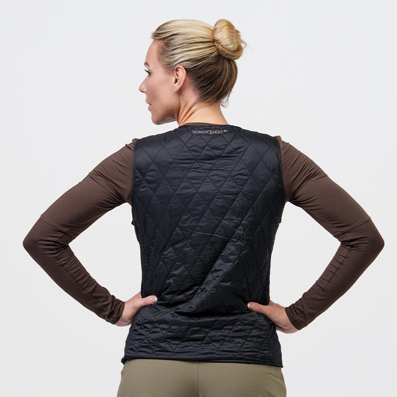 A person wearing a black, quilted NordicHeat vest over a brown sweater. The vest is seen from behind and the person has gathered their hair into a bun.