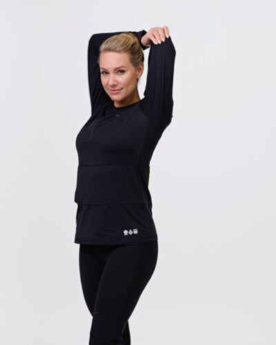 Woman stretches her arms wearing NordicHeat warm clothing in black that supports an active lifestyle. The garment is highlighted for functionality and comfort during physical activity. No text is visible.