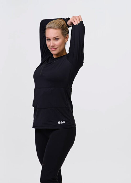 Woman stretches her arms wearing NordicHeat warm clothing in black that supports an active lifestyle. The garment is highlighted for functionality and comfort during physical activity. No text is visible.