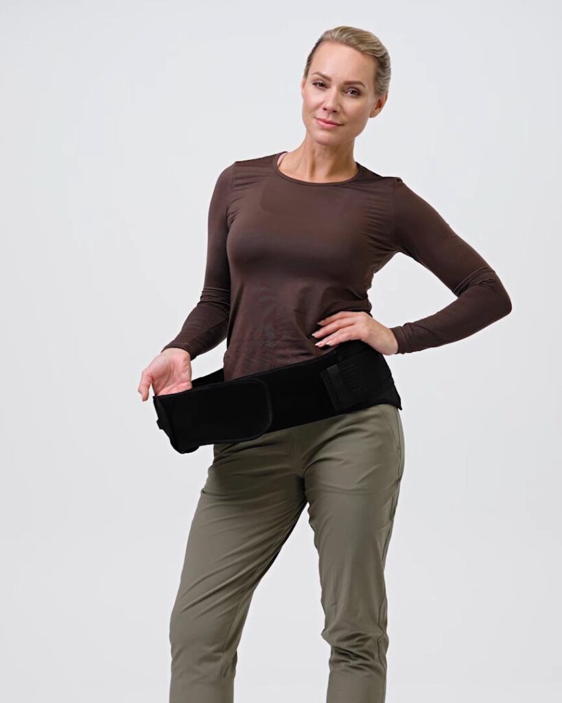A person wearing a NordicHeat heating vest, standing in a relaxed position. Green and brown clothing indicates active outdoor lifestyle. No visible text present.