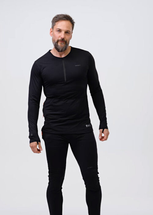 A man wearing black NordicHeat thermal clothing stands upright in a neutral, bright studio environment. The outfit consists of a long-sleeved shirt and pants designed for warmth.