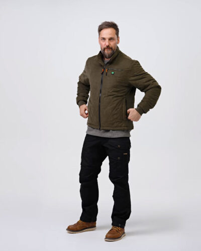 A person is wearing an olive green jacket with visible pockets, black pants and brown shoes on a neutral background. The jacket is the central element.