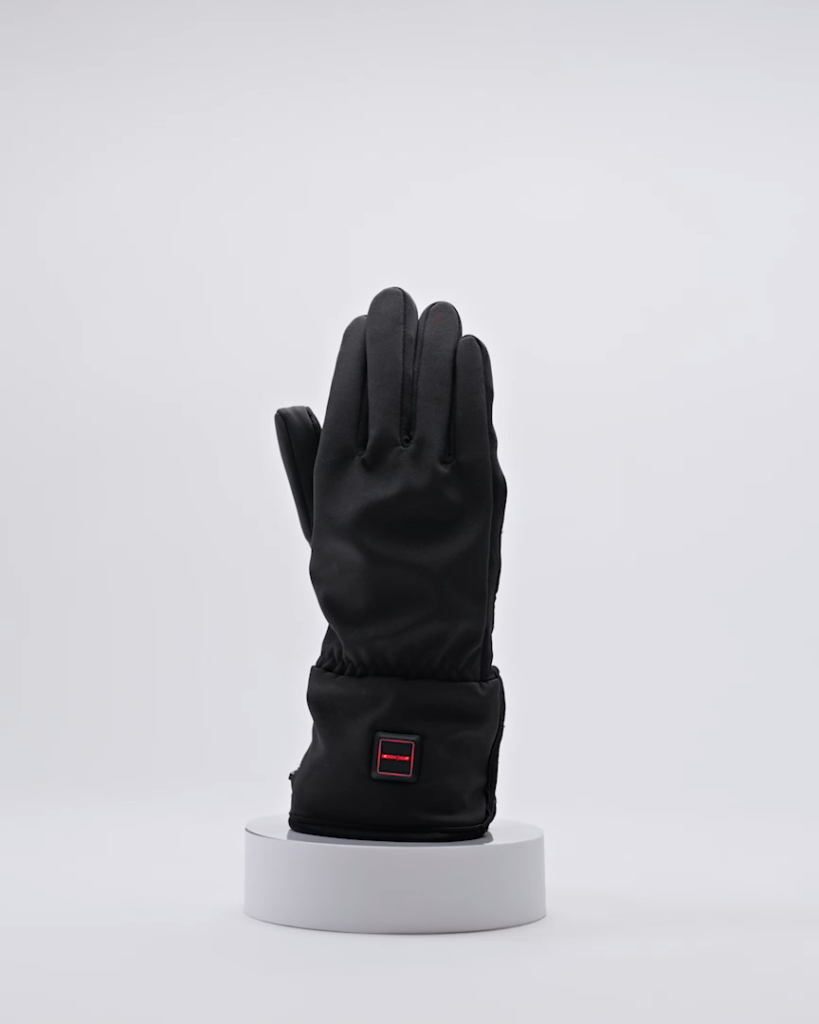 A black glove with heating function stands upright on a round white platform. The back of the glove has a visible red button. The background is white.