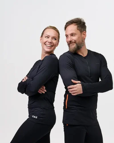Two people wearing black NordicHeat warm clothing stand back to back and smile, against a neutral background, with a focus on comfort and functionality.