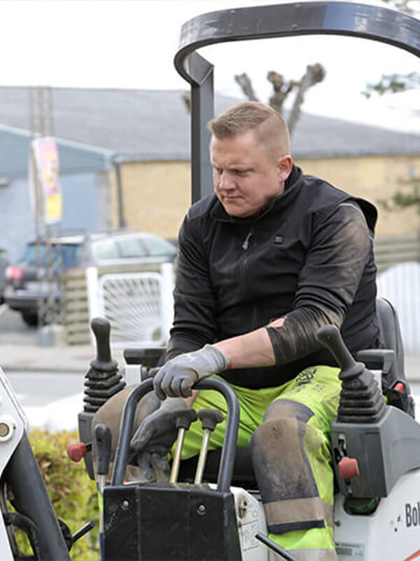 A person wearing NordicHeat thermal clothing works on a Bobcat in a construction site. The clothing ensures comfort and freedom of movement in active outdoor environments. No visible text.