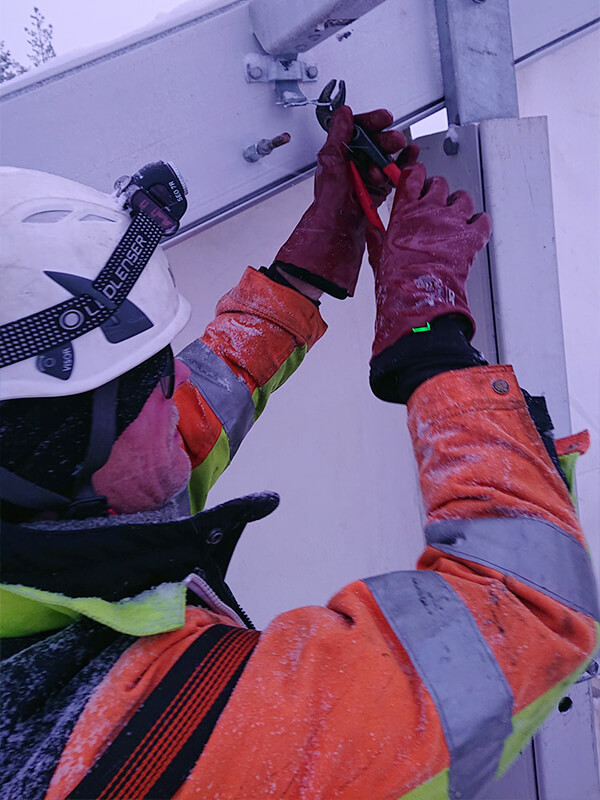 Working with Olight headlamp and warm garments adjusting a metal structure in cold weather, wearing protective helmet and gloves. Active lifestyle is supported by NordicHeat products.