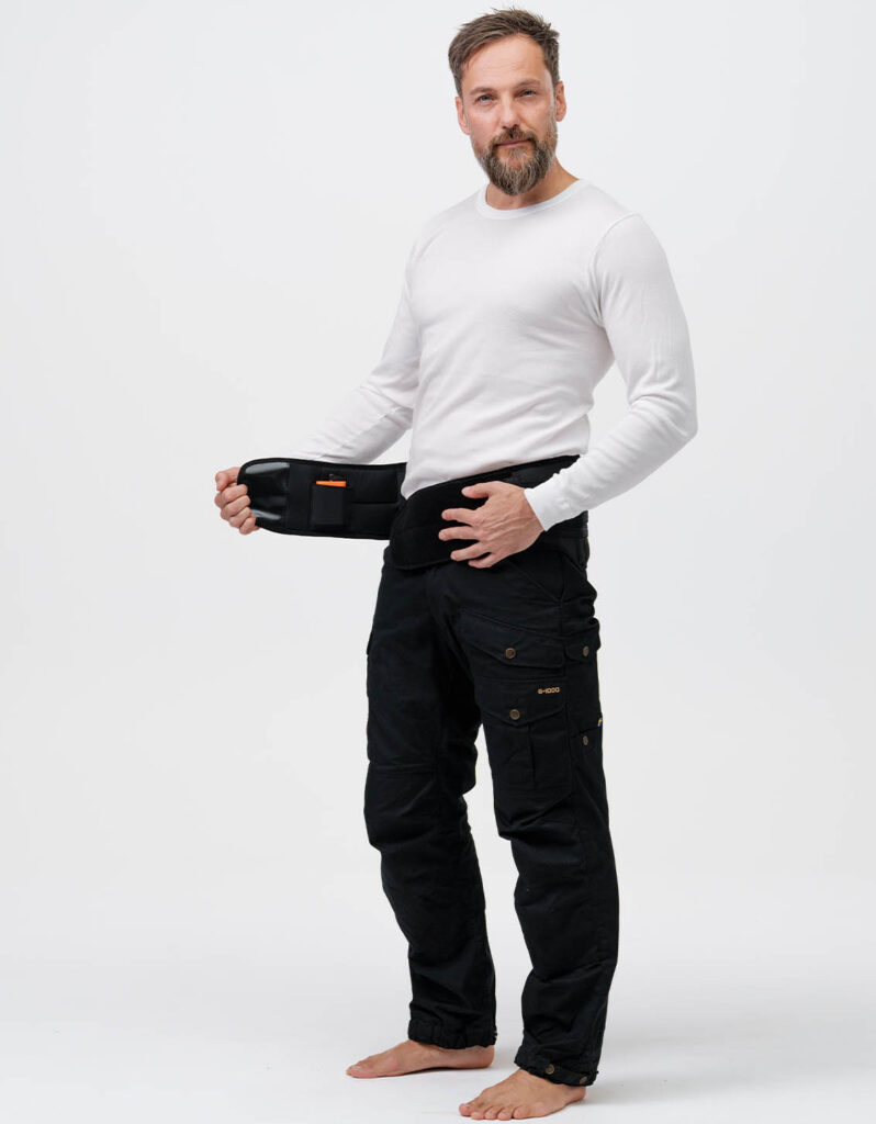 A person demonstrates an adjustable belt warmer from NordicHeat, wearing practical outdoor clothing. The label on the belt indicates its functionality in active lifestyle. Visible text: "E-ODD".