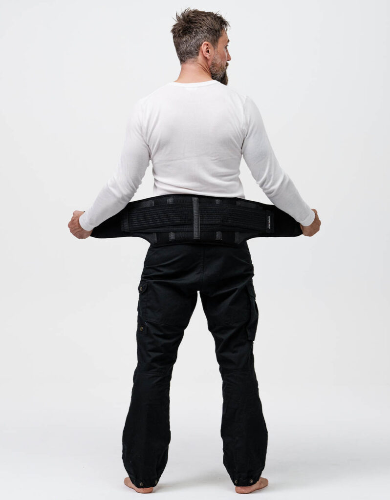A man dressed in a white shirt and black pants adjusts a black NordicHeat thermal garment, ideal for active lifestyles. No visible text.
