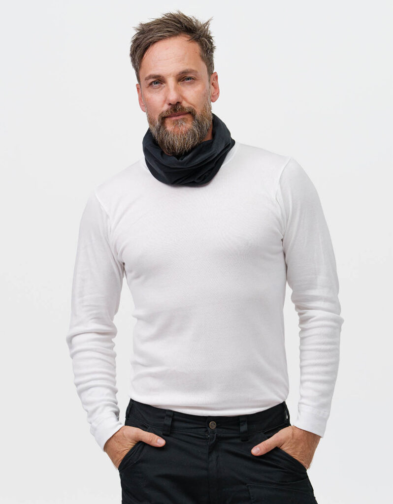 Person wearing a white sweater and black scarf standing casually with hands in pockets. Focus on NordicHeat's insulating warm clothing for an active lifestyle. No visible text.