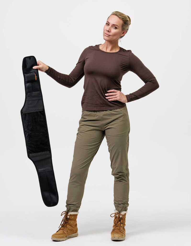 A person shows a black heatable body support from NordicHeat, wearing casual, practical clothing. The product supports an active lifestyle by offering warmth and comfort in motion.