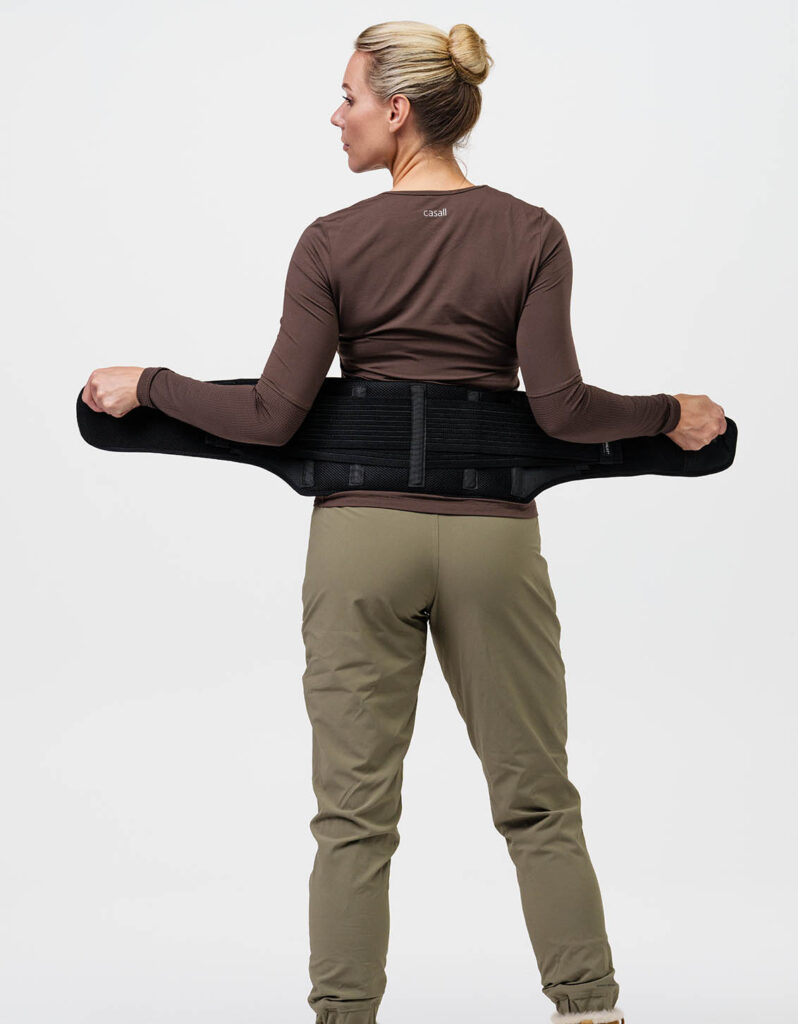 A person wearing thermal clothing adjusts a back belt for comfort and support in an active lifestyle. Text: "casall".