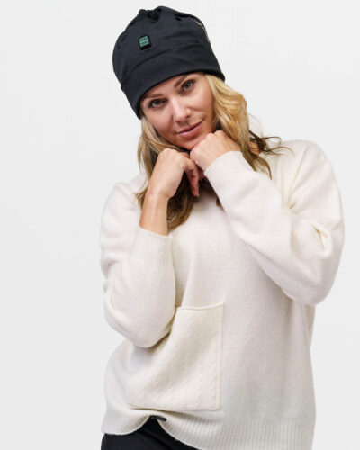 Person wears black NordicHeat warming beanie suitable for an active lifestyle. The cap has a green logo on the front. The person is dressed in a light sweater.