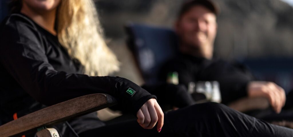 Person wearing black NordicHeat warm clothing leans relaxed in a chair with a focus on the wrist tag, in an outdoor context that emphasizes an active lifestyle.
