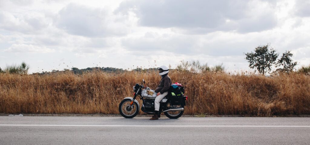 Motorcyclist wearing NordicHeat helmet and jacket pauses at roadside, surrounded by nature, symbolizing active lifestyle with effective thermal clothing combinations. No visible text.